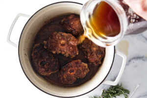 Pouring broth in a pot of oxtails.