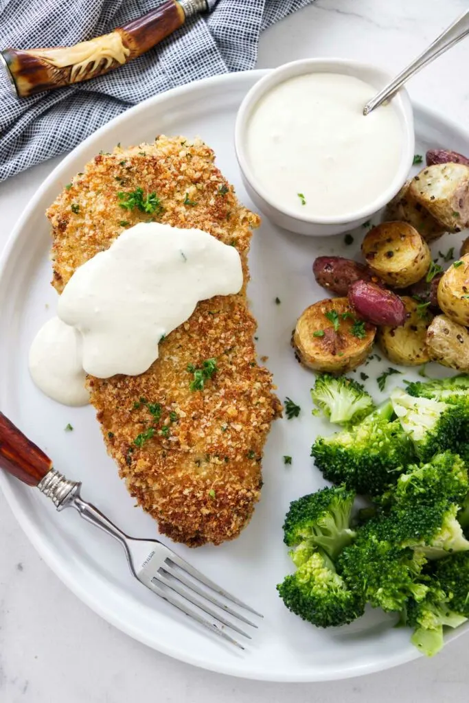 Panko crusted chicken on a plate with potatoes and broccoli.