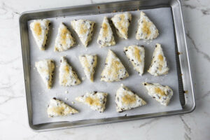 Adding the sliced scones to a baking sheet and topping them with cream and coarse sugar.