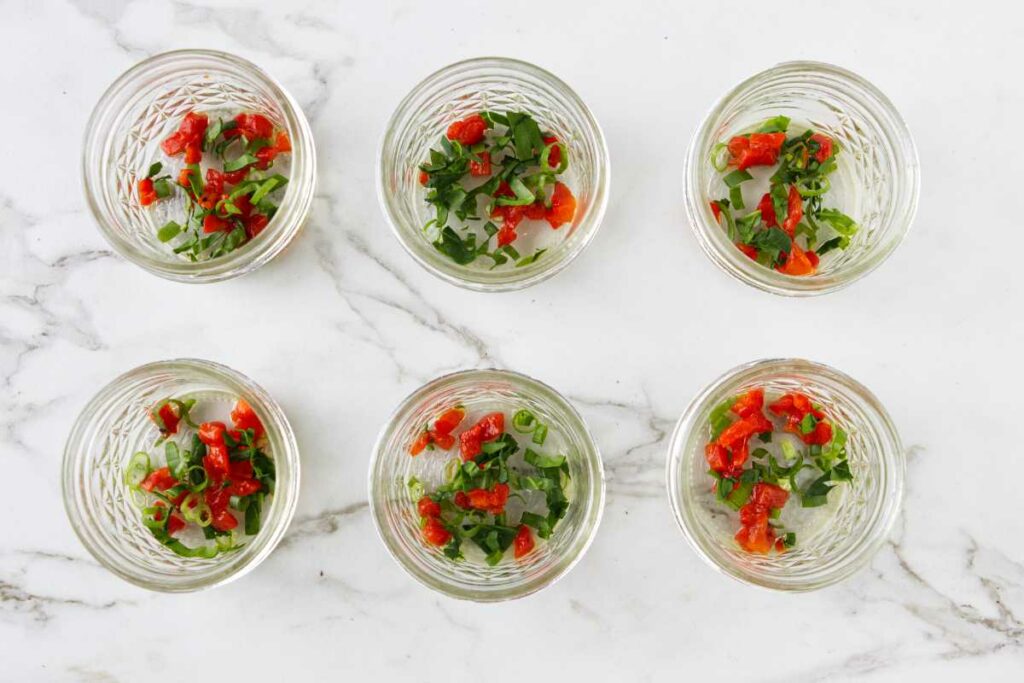 Adding bell peppers, green onions, and spinach to the bottom of six small mason jars.