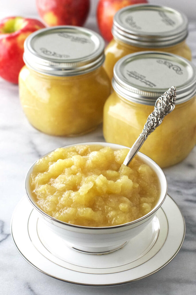 Mason jars filled with applesauce next to a dish of applesauce.