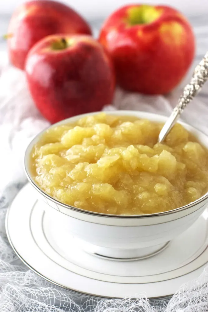 A dish of chunky applesauce with apples in the background.