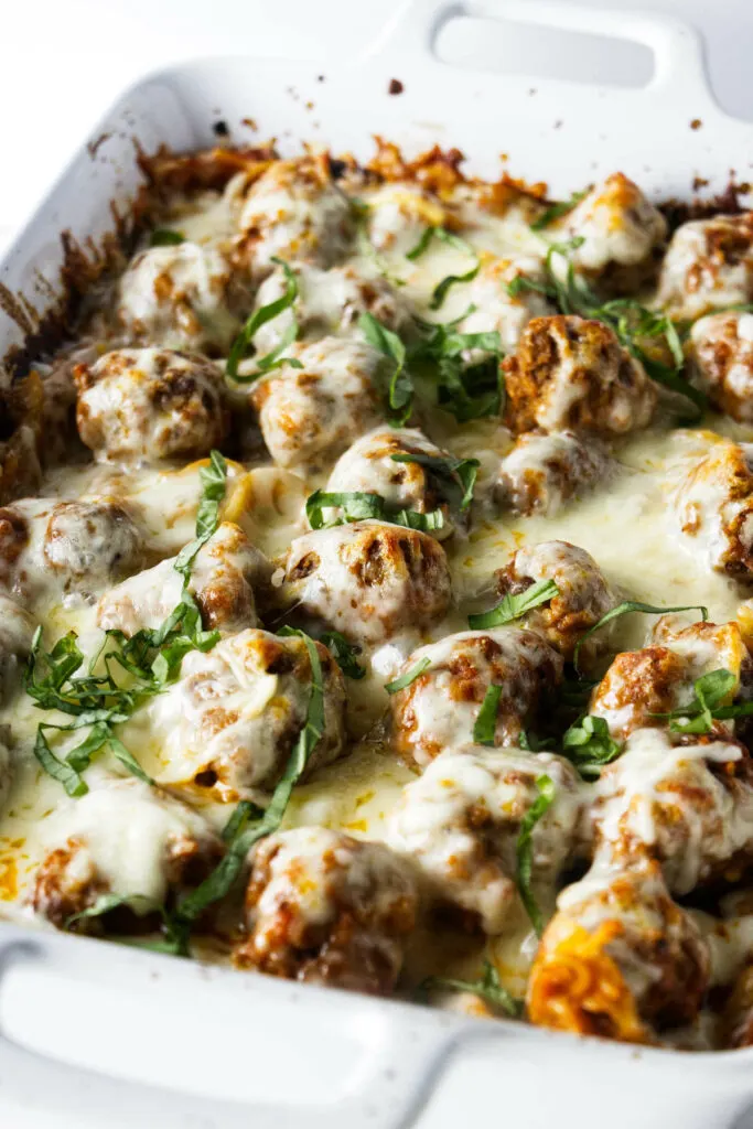 Baked spaghetti in a casserole dish topped with meatballs and melted cheese.