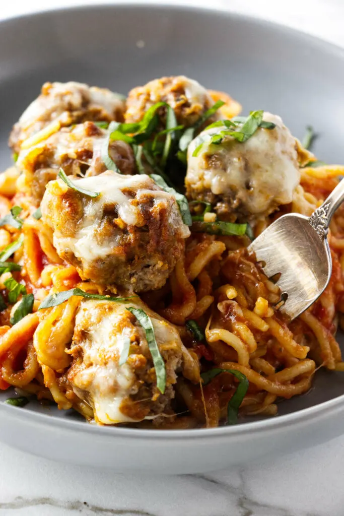 A bowl filled with a serving of cheesy baked spaghetti and meatballs.