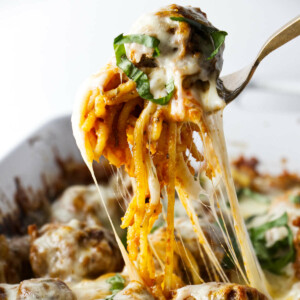 A serving of baked spaghetti with stretchy melted cheese and a meatball.