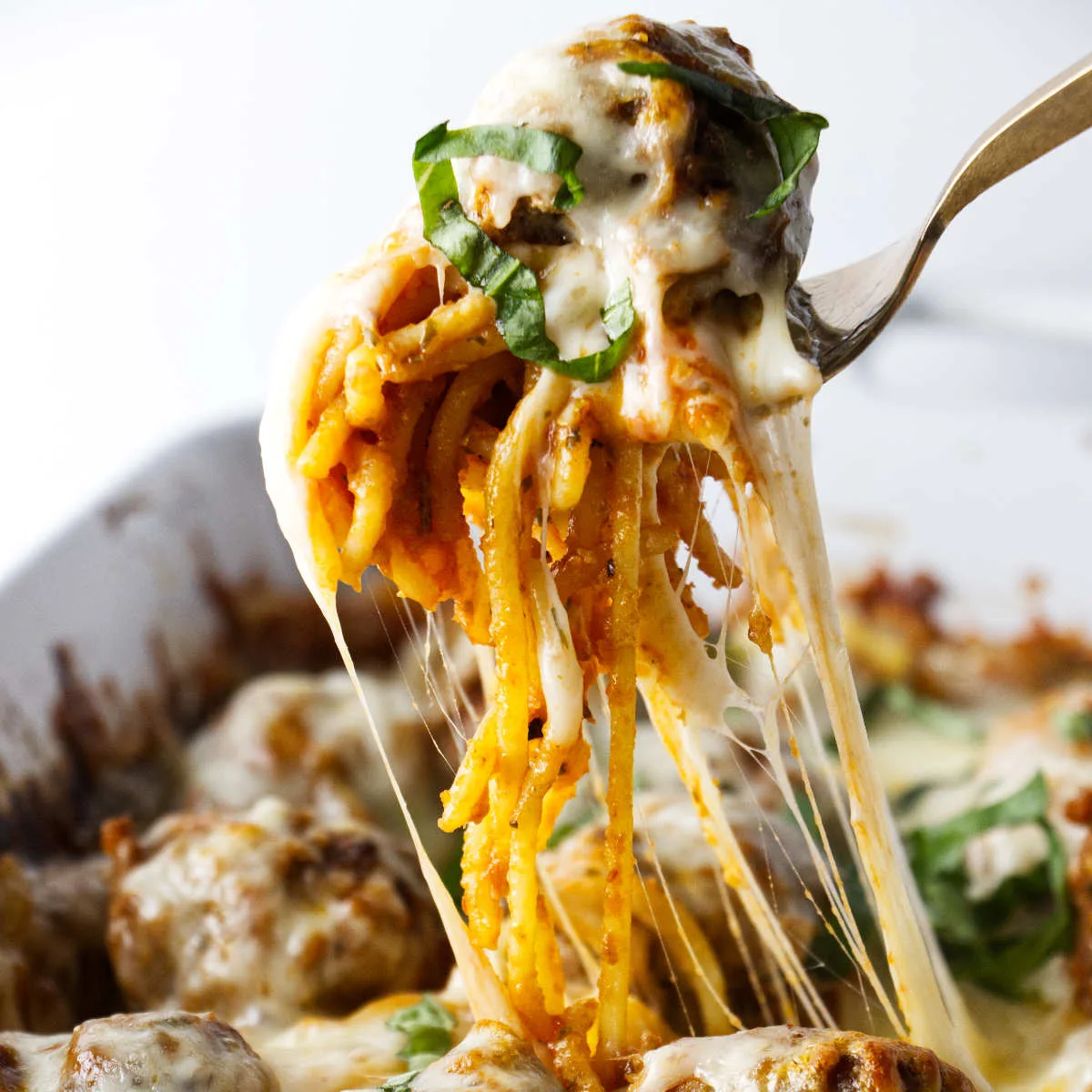 A serving of baked spaghetti with stretchy melted cheese and a meatball.