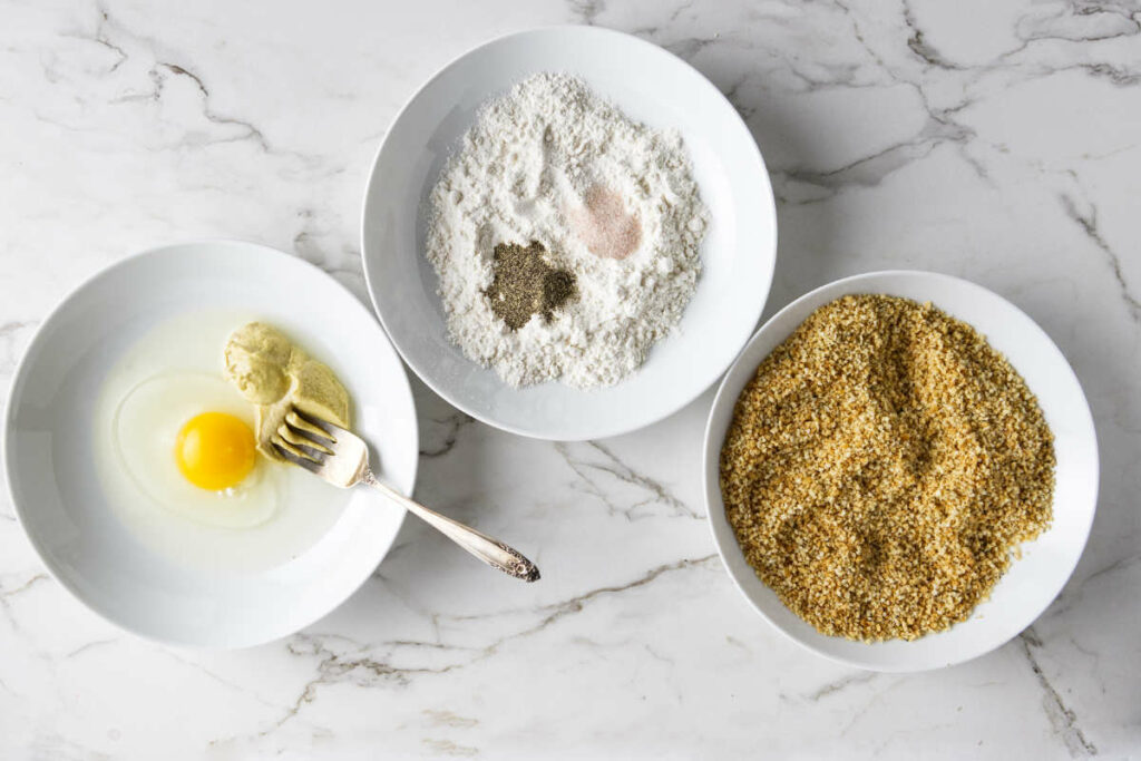 Three dishes with ingredients to coat the chicken cordon blue: egg wash, flour, and panko coating.