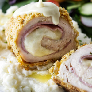 Pouring sauce over a serving of chicken cordon blue.