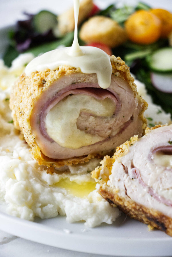 Pouring sauce over a serving of chicken cordon blue.