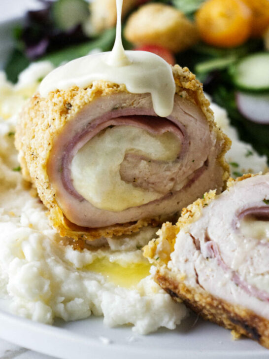 Pouring sauce over a serving of chicken cordon blue.