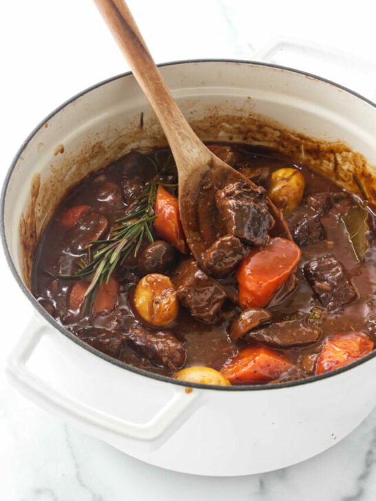 A wooden spoon in a Dutch oven with beef stew.