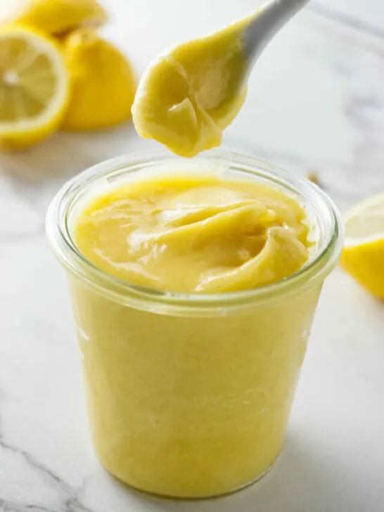 A spoon scooping thick lemon curd out of a jar.