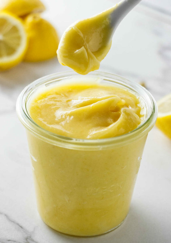 A spoon scooping thick lemon curd out of a jar.