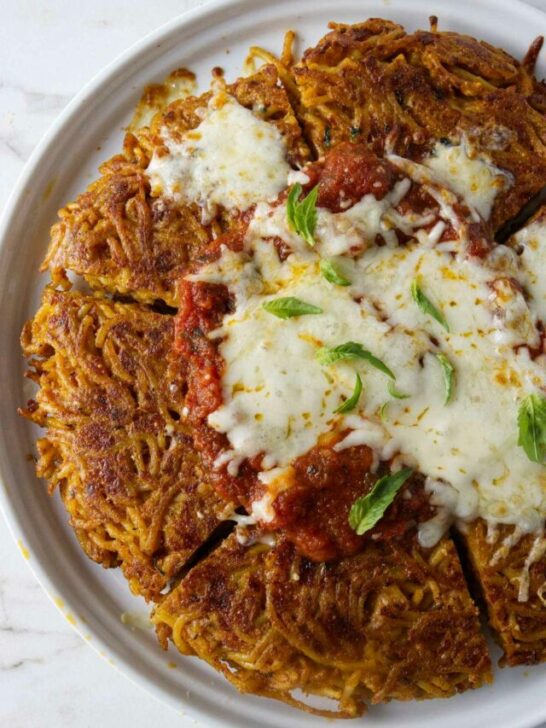 A serving plate with fried spaghetti topped with marinara sauce and cheese.