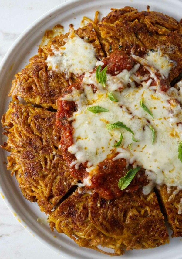 A serving plate with fried spaghetti topped with marinara sauce and cheese.