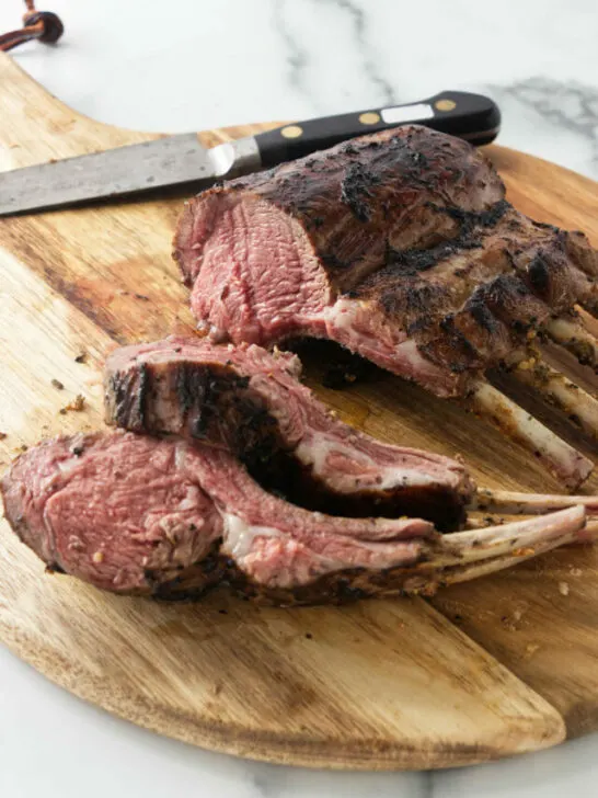 A grilled rack of lamb on a wooden cutting board.