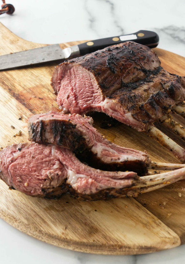 A grilled rack of lamb on a wooden cutting board.