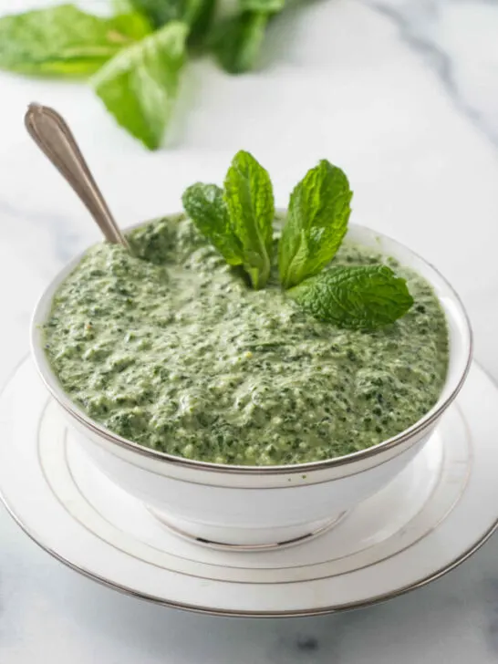 Mint sauce in a dish next to fresh mint leaves.