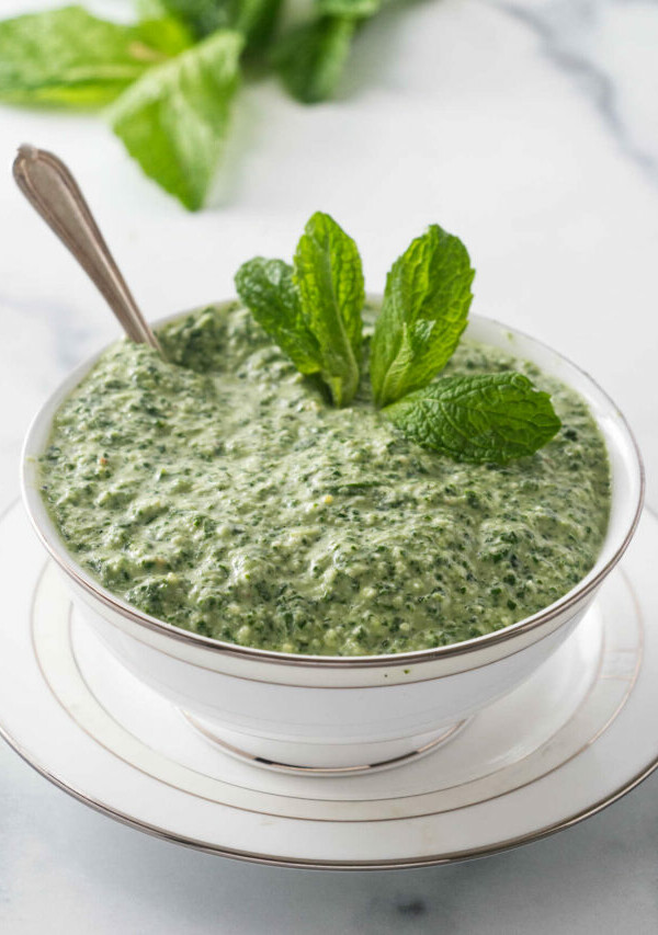 Mint sauce in a dish next to fresh mint leaves.