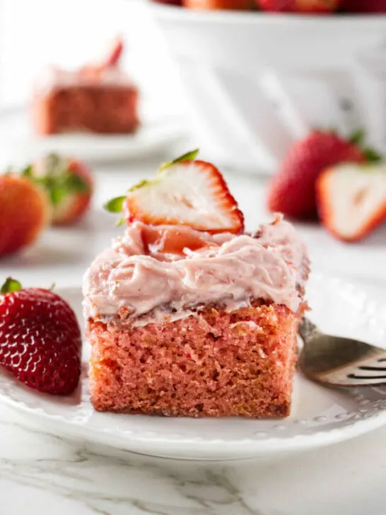 A slice of strawberry jam cake next to a fork and fresh strawberries.