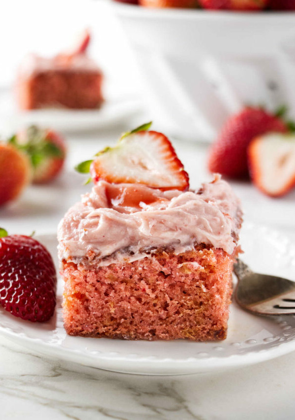 A slice of strawberry jam cake next to a fork and fresh strawberries.