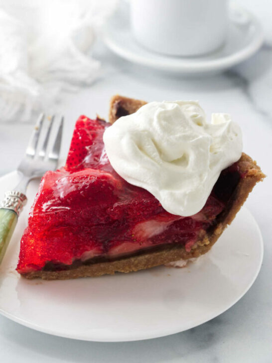 A slice of strawberry pie made with jello in front of a cup of coffee.