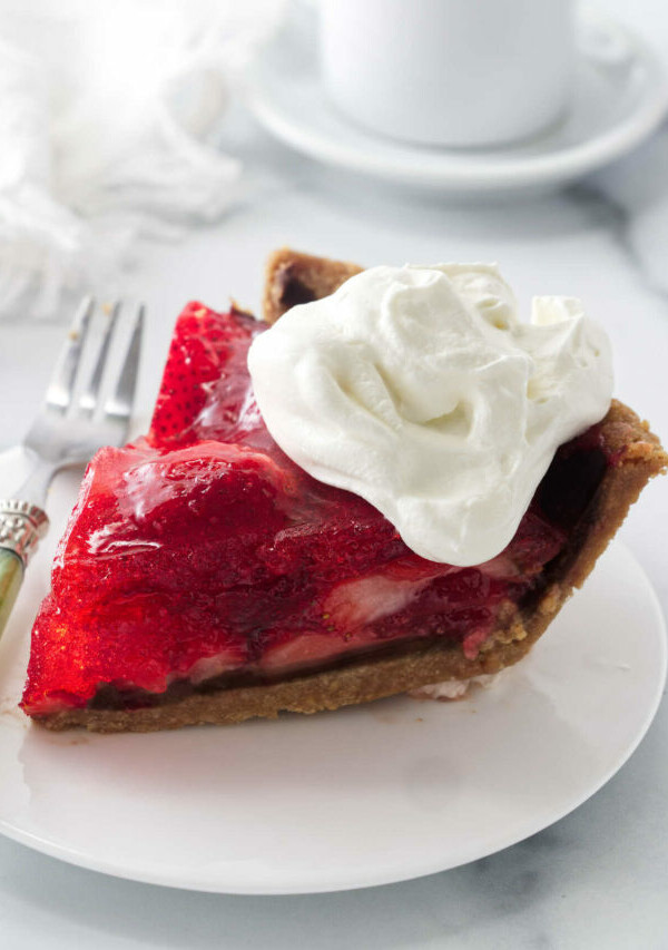 A slice of strawberry pie made with jello in front of a cup of coffee.