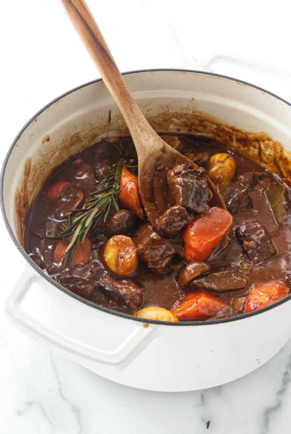 A wooden spoon in a Dutch oven with beef stew.