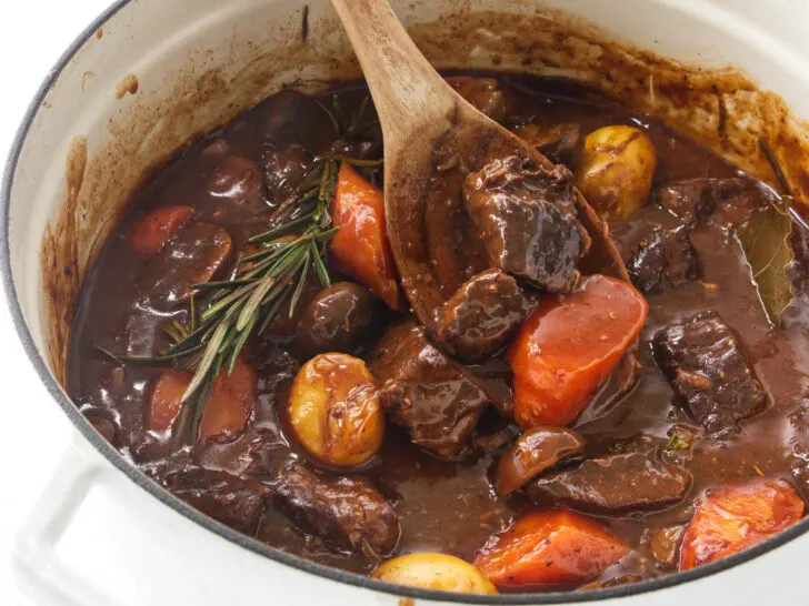A wooden spoon in a Dutch oven with beef stew.