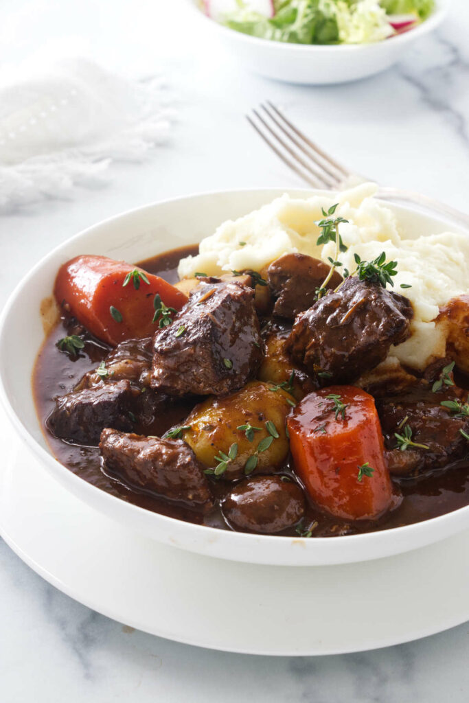 A bowl of Dutch oven beef stew with mashed potatoes.