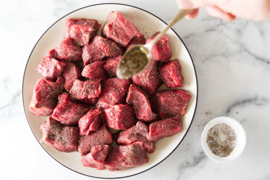 Seasoning chunks of beef with salt and pepper.