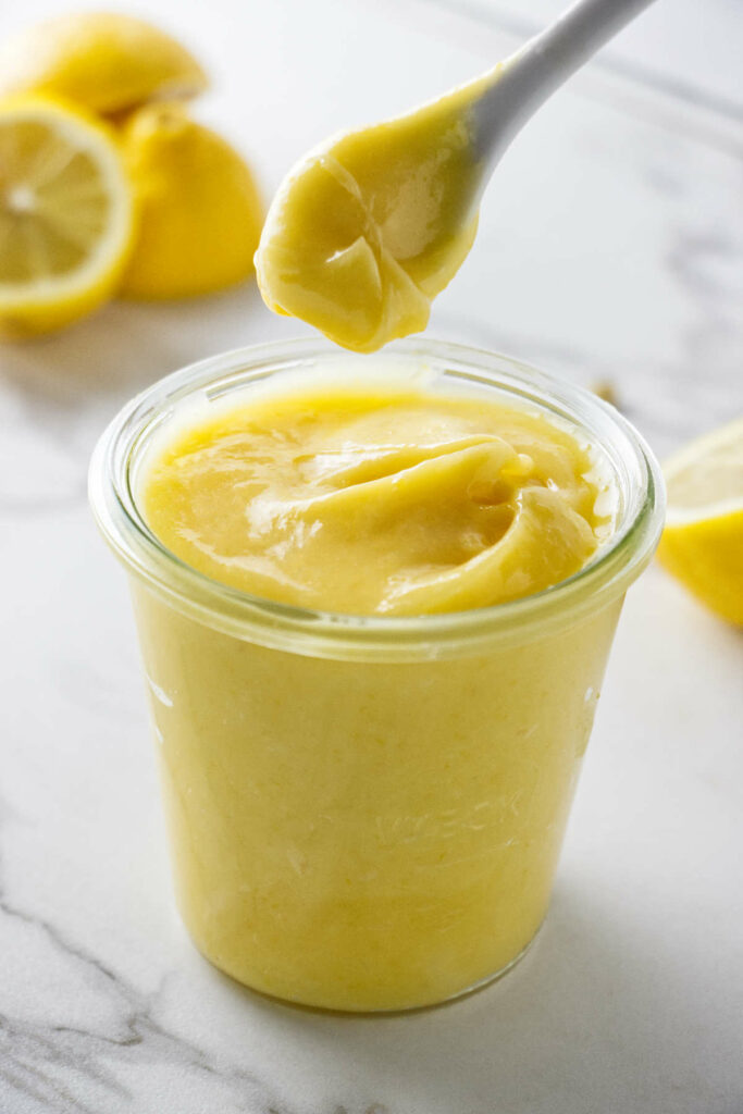 A spoon scooping thick lemon curd out of a jar.