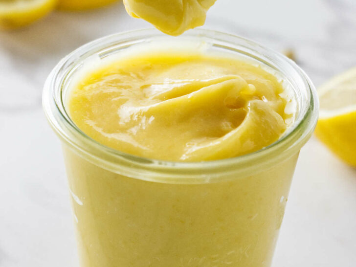 A spoon scooping thick lemon curd out of a jar.