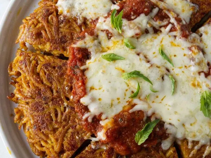 A serving plate with fried spaghetti topped with marinara sauce and cheese.