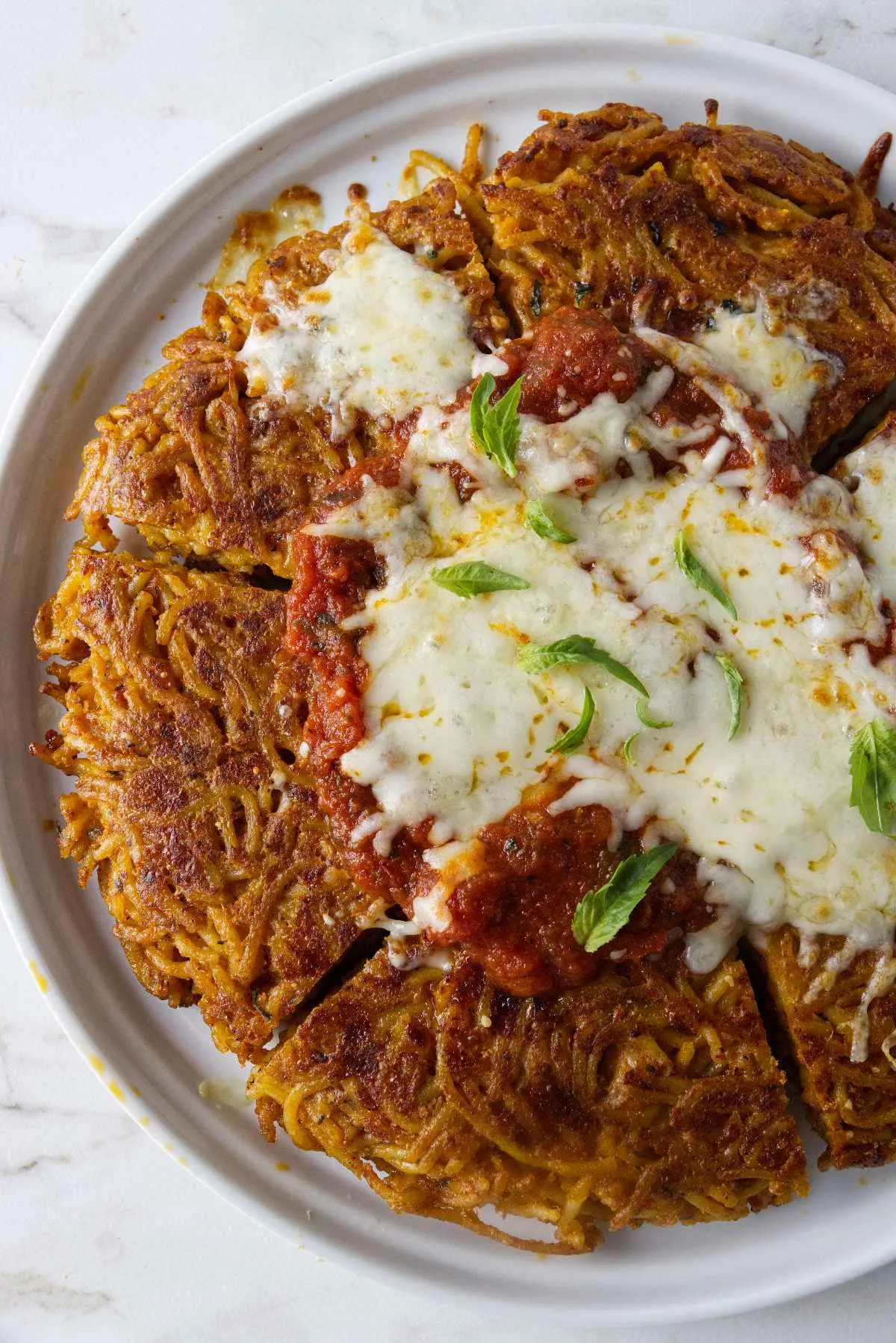 A serving plate with fried spaghetti topped with marinara sauce and cheese.