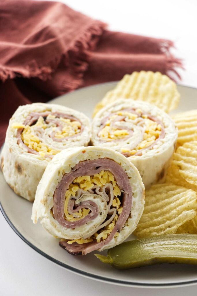 Ham and turkey pinwheels on a plate with chips and pickles.