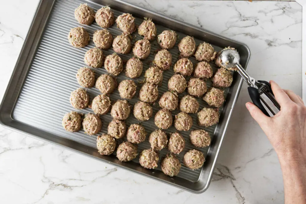 Placing turkey meatballs on a baking pan.