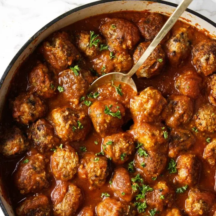 A spoon scooping turkey meatballs out of a pan.