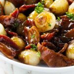 A serving dish filled with caramelized pearl onions and bacon.