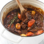 A pot of Dutch oven beef stew with a wooden spoon.