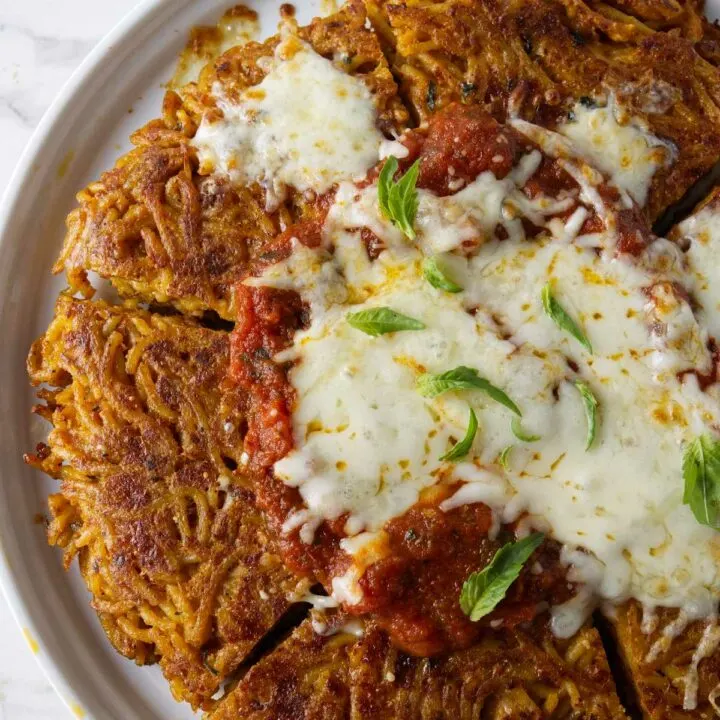 Fried spaghetti on a serving plate topped with marinara sauce and cheese.