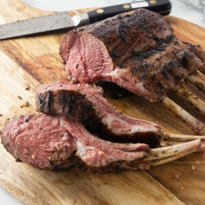 A grilled rack of lamb on a wooden cutting board.