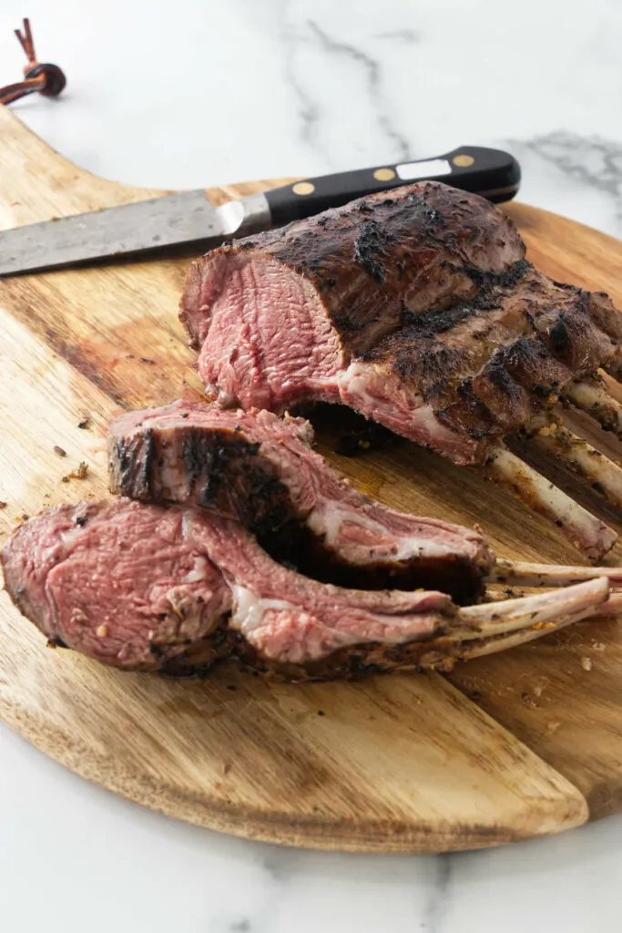 A grilled rack of lamb on a wooden cutting board.
