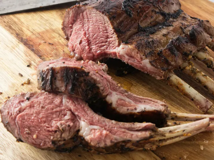 A grilled rack of lamb on a wooden cutting board.