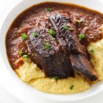A bowl filled with short ribs on a bed of polenta.