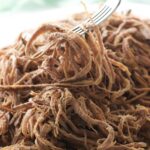 A slow cooker tri tip roast shredded with a fork.