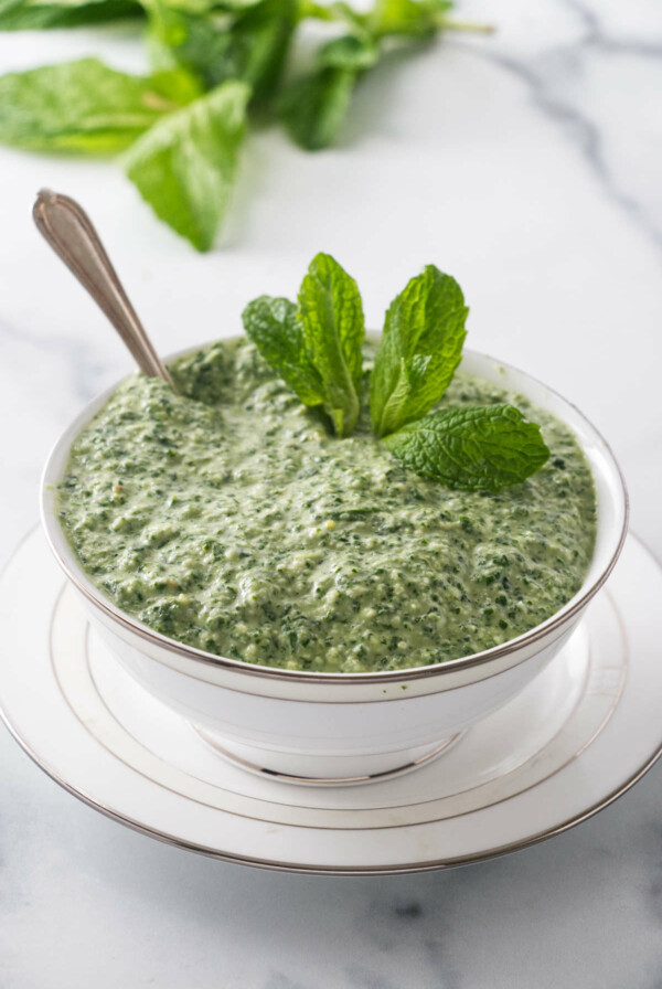 Mint sauce in a dish next to fresh mint leaves.