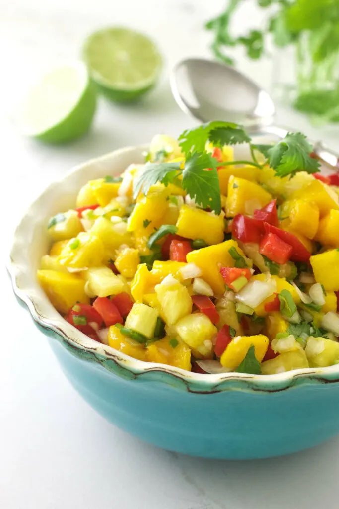 Pineapple mango salsa in a dish with limes in the background.