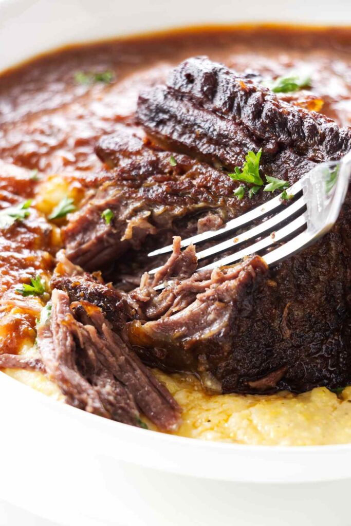 A fork shredding the beef off a spicy short rib.