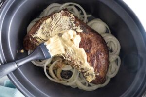 Brushing Dijon mustard over a tri tip in a slow cooker.